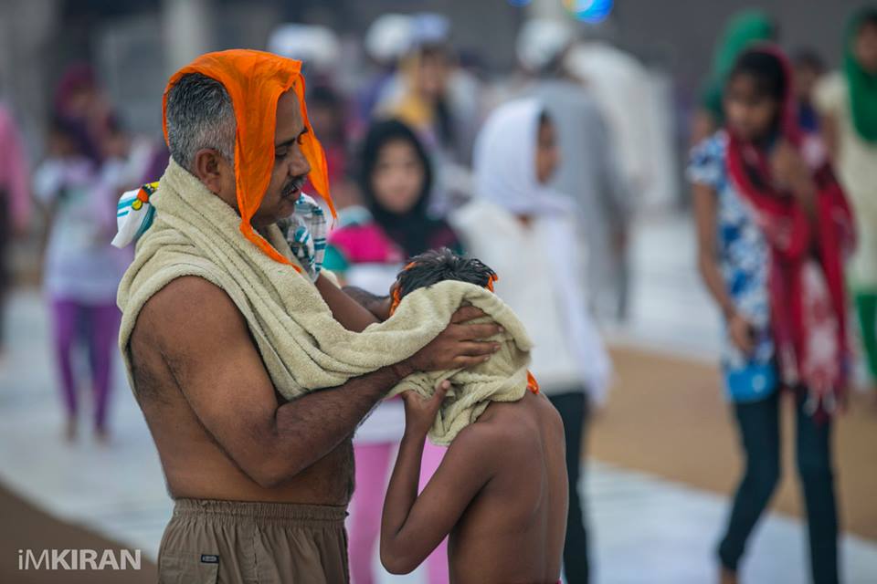 a father wiping his son dry after a dip in the holy pool