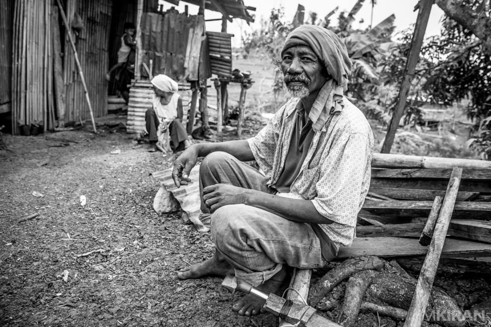 They have a beautiful way of life.. easy and peaceful. Narciso sitting while having his tobacco roll and parang (knife) by his side. At the background is his home. A shelter they build after the recent typhoon destroyed everything. 